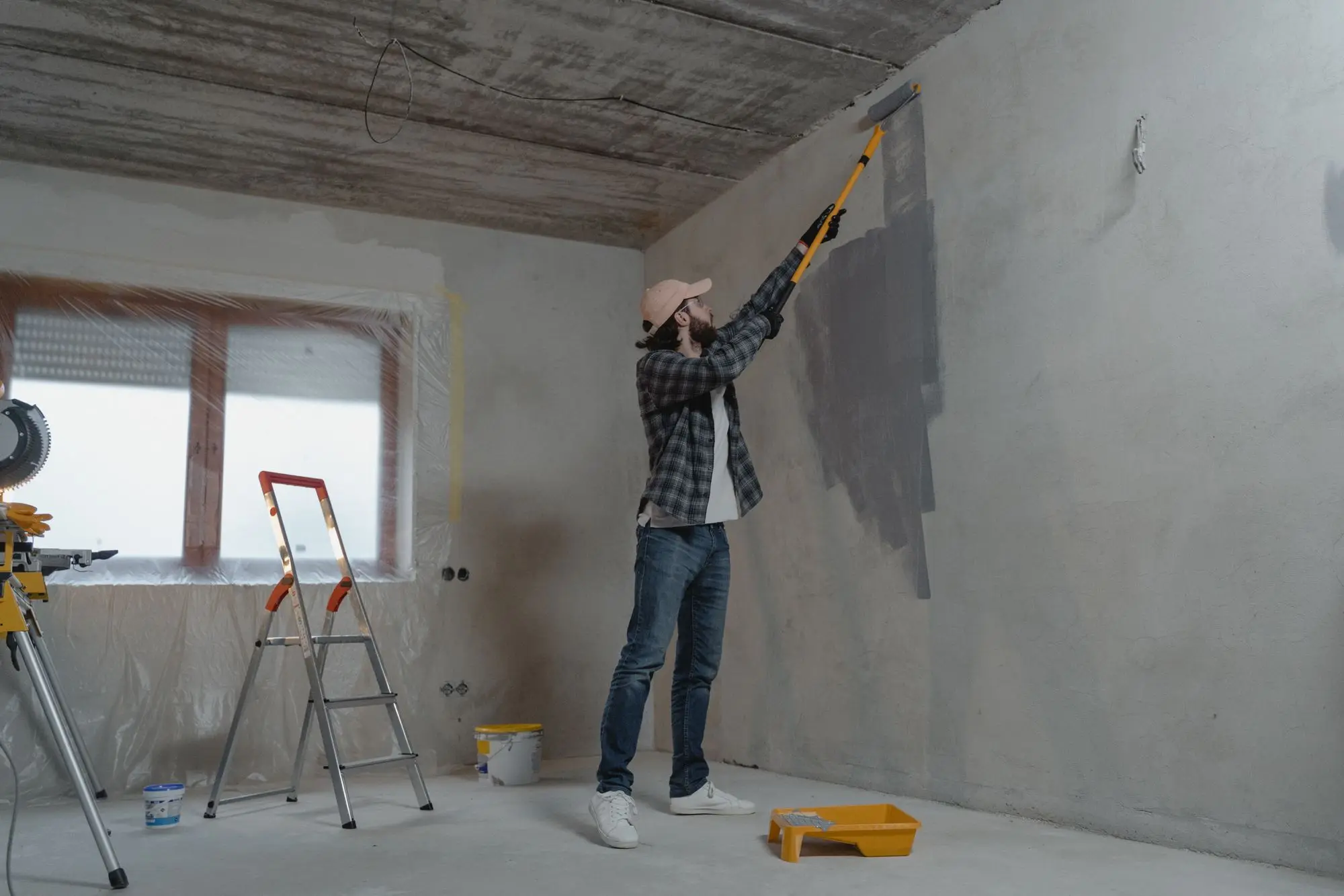 Tradesperson using an extension roller to repaint the bare walls of an emptied premises before the lease is handed back